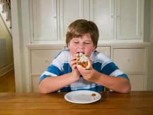 Overweight boy (10-11) sitting at table eating hot dog
